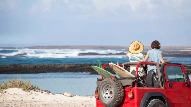 A couple at the beach in their red jeep with surfboards